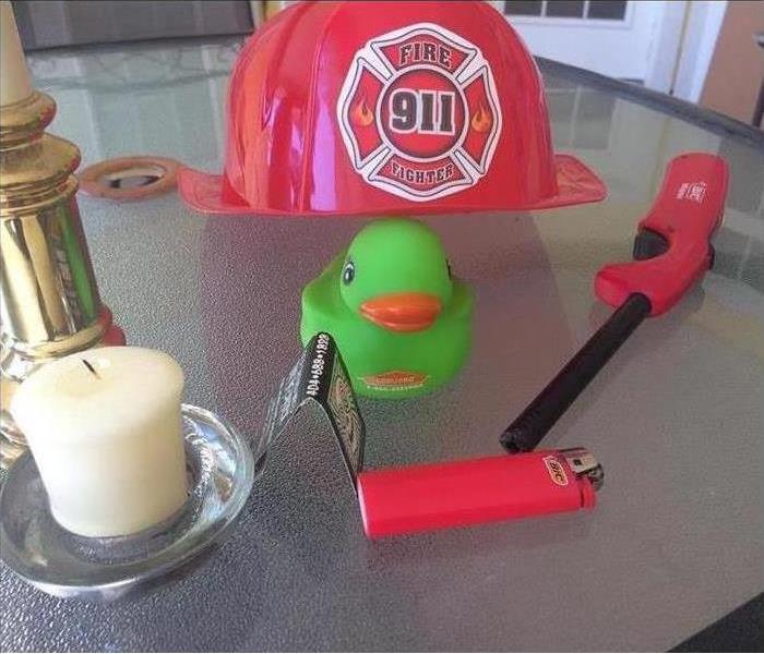 Lighters, a rubber duck, a candle, and a Firefighter helmet on a table. 
